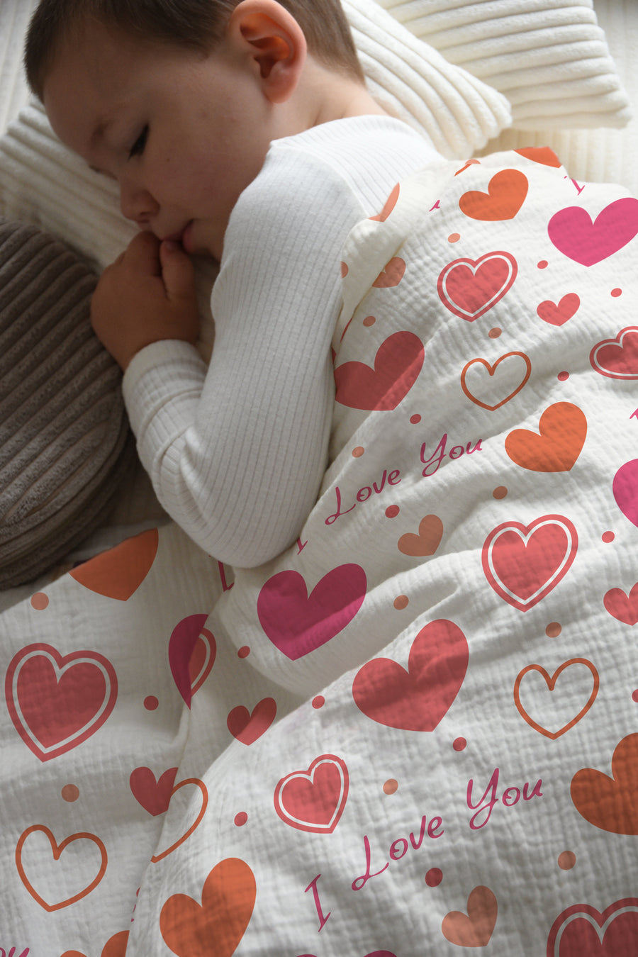 Junge schläft in Kinderbettwäsche „I love you" mit rosa Herzen in einem hellen Kinderzimmer