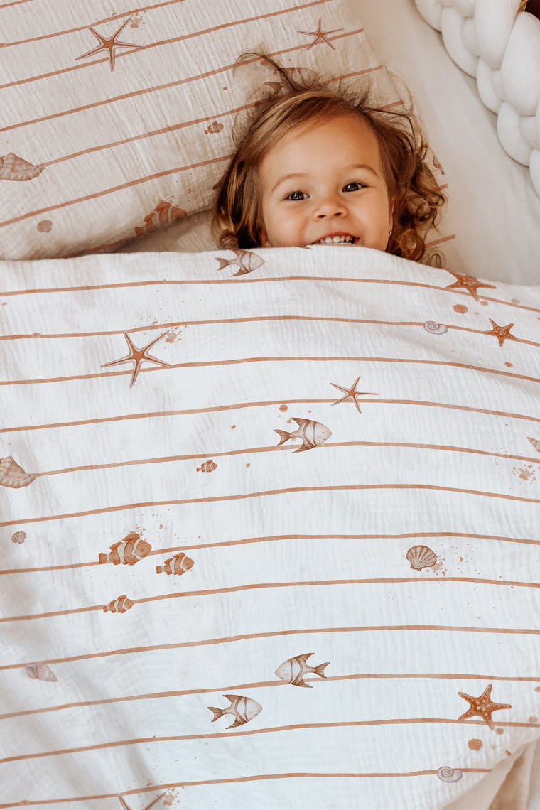 LESLIS Kinderbettwäsche „Kleine Seesterne" – Mädchen im Bett mit bezogener Bettdecke
