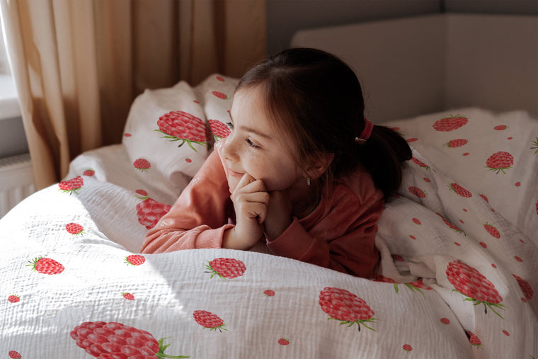 LESLIS Kinderbettwäsche „Himbeeren" – Mädchen im Bett mit bezogener Bettdecke