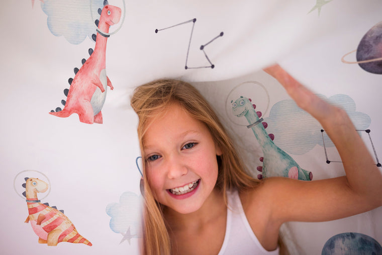 LESLIS Kinderbettwäsche „Dino Galaxy" – Mädchen im Kinderbett mit Dino- und Sterne-Motiv