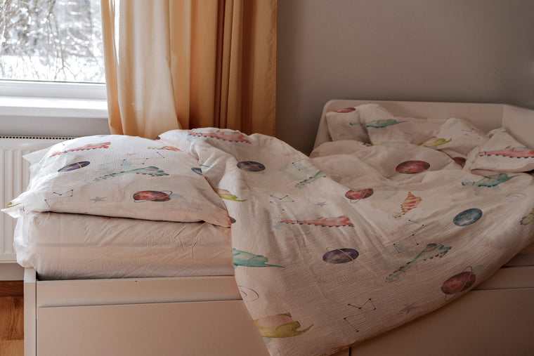 LESLIS Kinderbettwäsche „Dino Galaxy" – Kind im Bett mit bezogener Bettdecke
