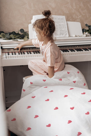 Mädchen lacht im Bett mit Kinderbettwäsche „Love" mit kleinen Herzchen