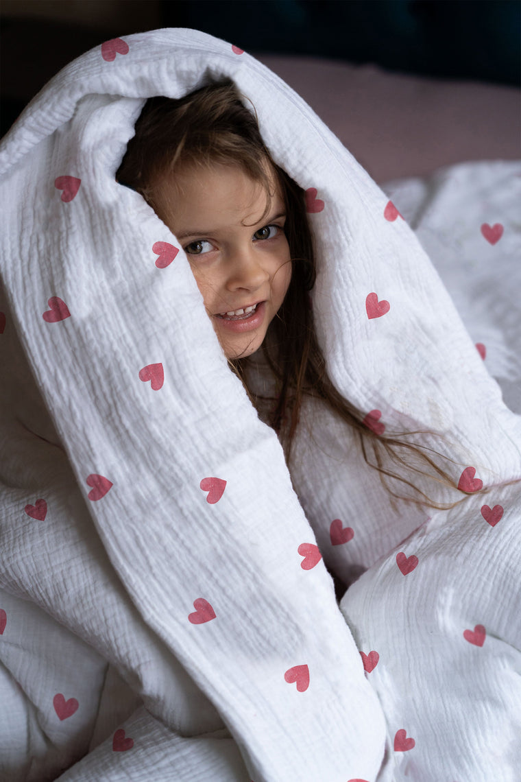 Mädchen im Bett mit Kinderbettwäsche „Love", viele kleine Herzchen in sanften Tönen