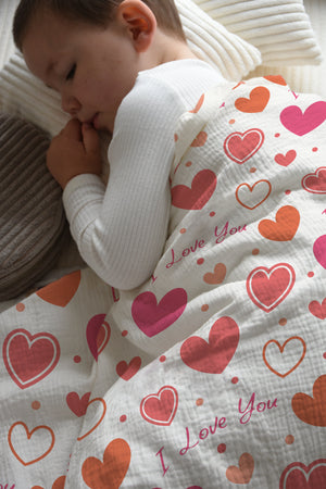 Junge schläft in Kinderbettwäsche „I love you" mit rosa Herzen in einem hellen Kinderzimmer