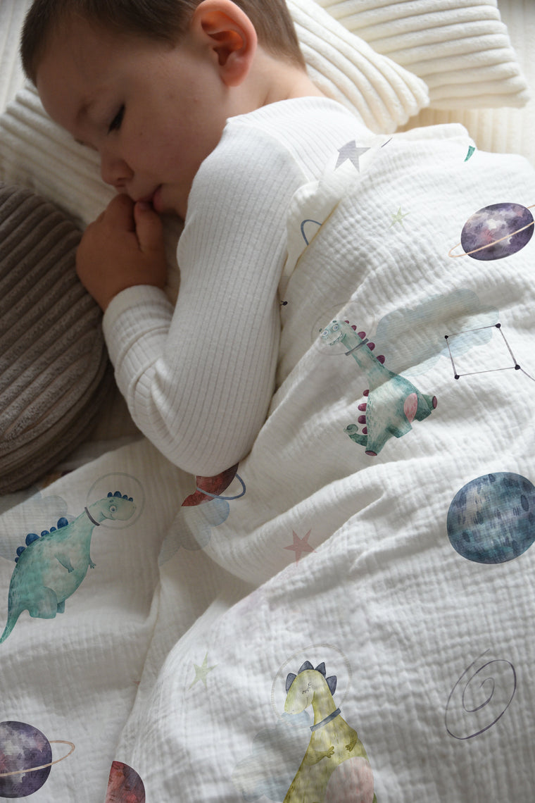 LESLIS Kinderbettwäsche „Dino Galaxy" – Junge im Bett mit bezogener Bettdecke