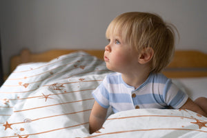 LESLIS Kinderbettwäsche „Kleine Seesterne" – Junge im Bett mit bezogener Bettdecke