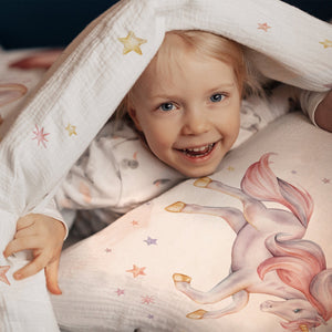 Mädchen lacht im Bett mit Kinderbettwäsche „Sternen Einhorn" mit Einhörnern