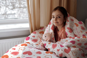 Mädchen im Bett mit Kinderbettwäsche „I love you", Herzen und Punkte in Rosa und Orange