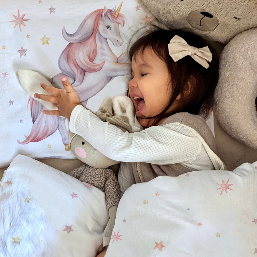Mädchen kuschelt im Bett mit Einhorn-Kinderbettwäsche „Sternen Einhorn"