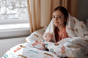 LESLIS Kinderbettwäsche „Am Meer" – Mädchen im Bett mit bezogener Bettdecke