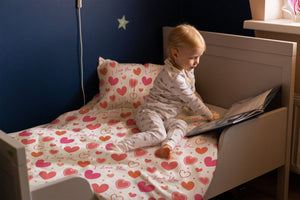 Lachendes Mädchen im Bett mit der Herzchen-Kinderbettwäsche „I love you" in zartem Rosa