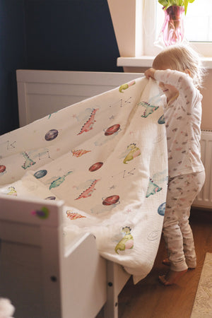 LESLIS Kinderbettwäsche „Dino Galaxy" – Mädchen im Bett mit bezogener Bettdecke