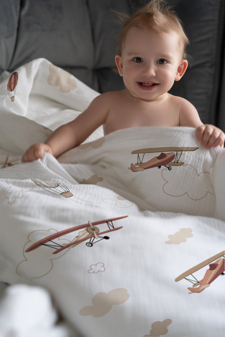 Fröhliches Kind im Bett mit Flugzeug-Kinderbettwäsche „Flugzeuge und Wolken"