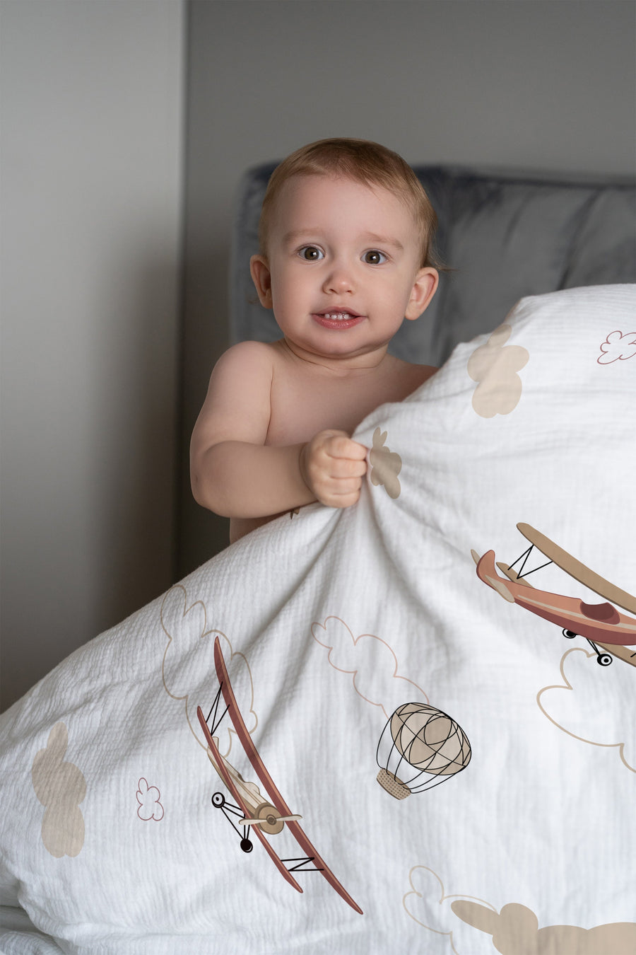 Lachendes Kind im Bett mit Kinderbettwäsche „Flugzeuge und Wolken" in Himmelblau